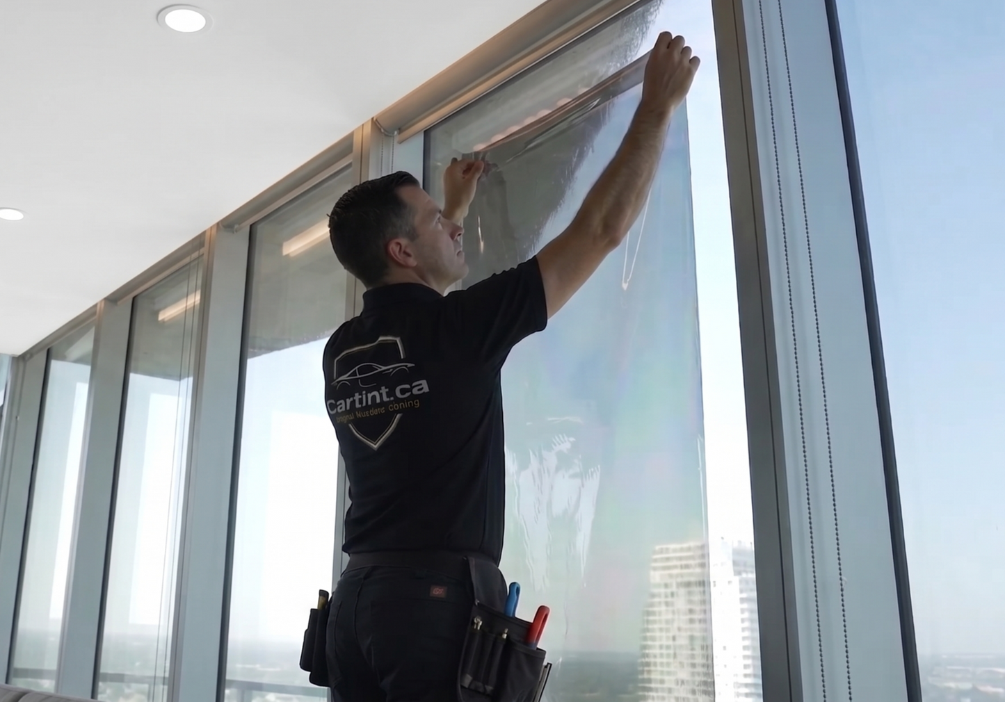 A professional Cartint  technician installing heat and glare reduction window tint film on large floor to ceiling windows in a high-rise apartment condo.
