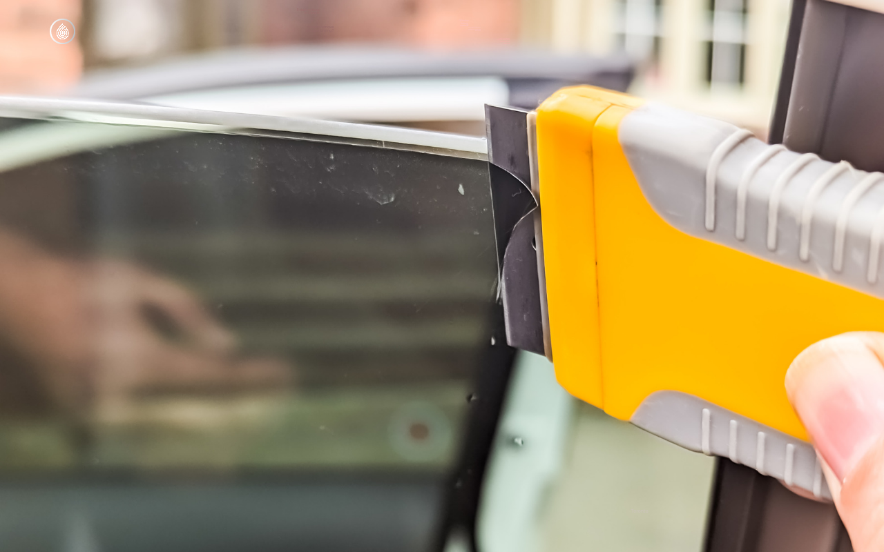Professional using a scraper to carefully remove window tinting, demonstrating the process of window tint removal. The image visually guides on how to remove window tint effectively. Car Tint, window tinting near me, window tint