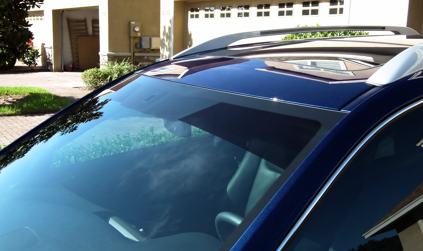 A dark blue SUV parked in a residential driveway, showcasing a premium windshield sun strip window tint installed across the top glass to block blinding sun glare and protect the dashboard