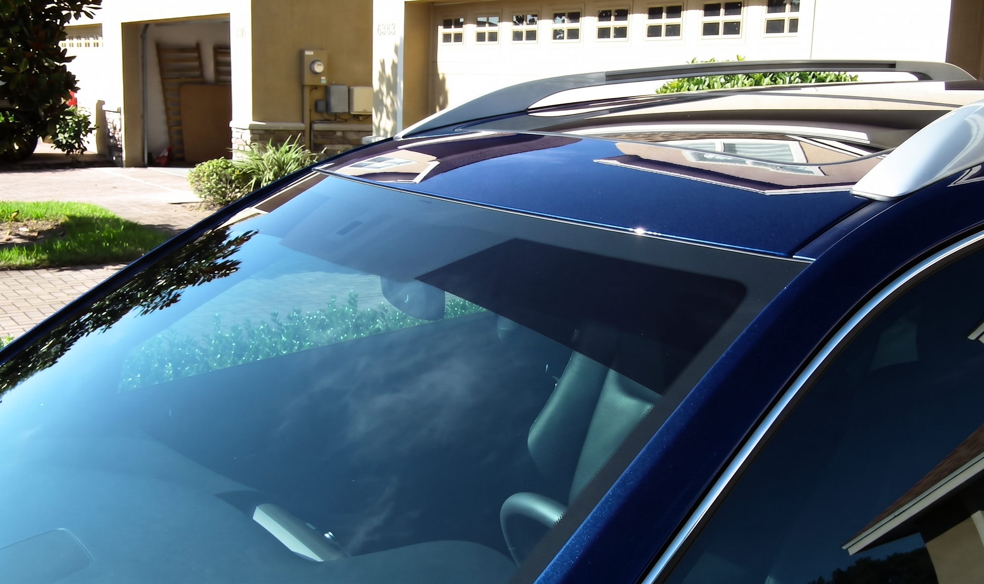 A dark blue SUV parked in a residential driveway, showcasing a premium windshield sun strip window tint installed across the top glass to block blinding sun glare and protect the dashboard